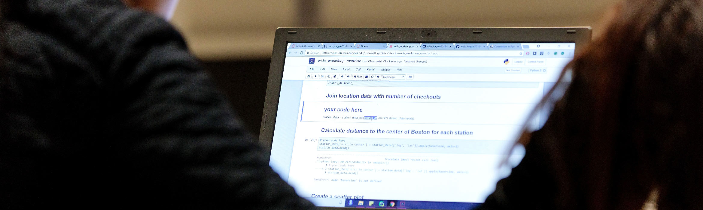 Blurry foreground of two women sitting next to each other with laptop in focus in front of them.