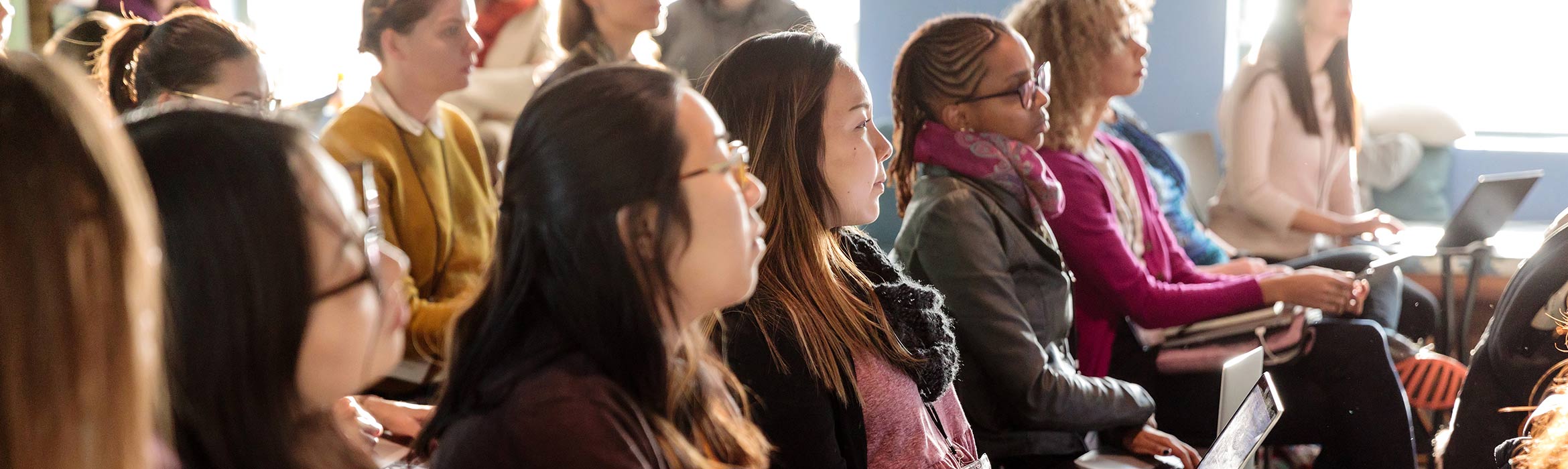 Women sitting in a row of chairs looking ahead.