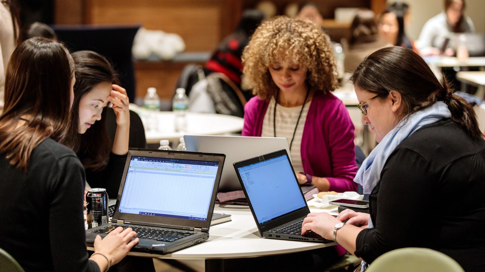 Four women sitting at a round table on their laptops